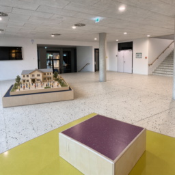 Das Foyer mit einer kleinen Miniatur-Schule auf der Holzplattform, umgeben von winzigen lustigen Menschenfiguren.